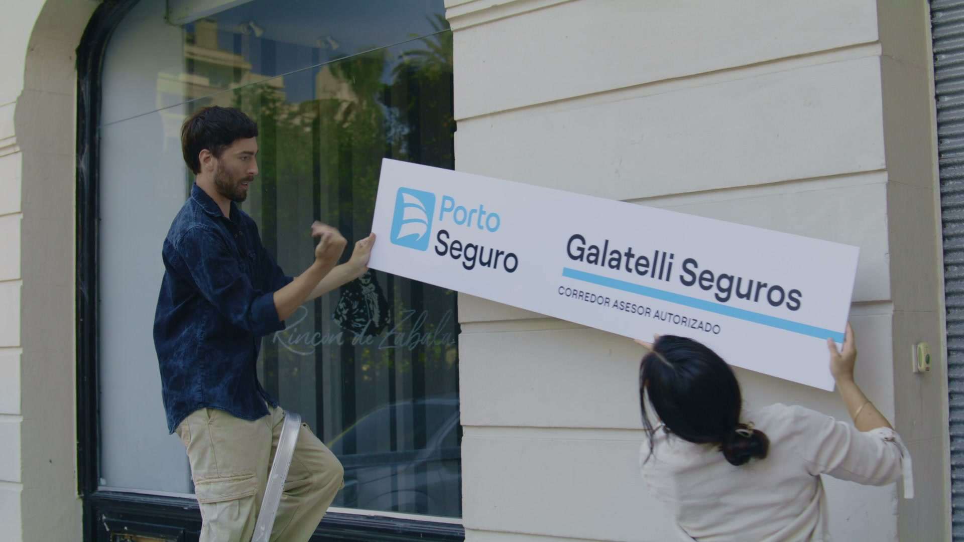 Dos personas colocando el cartel de Porto Seguro en el frente de una agencia