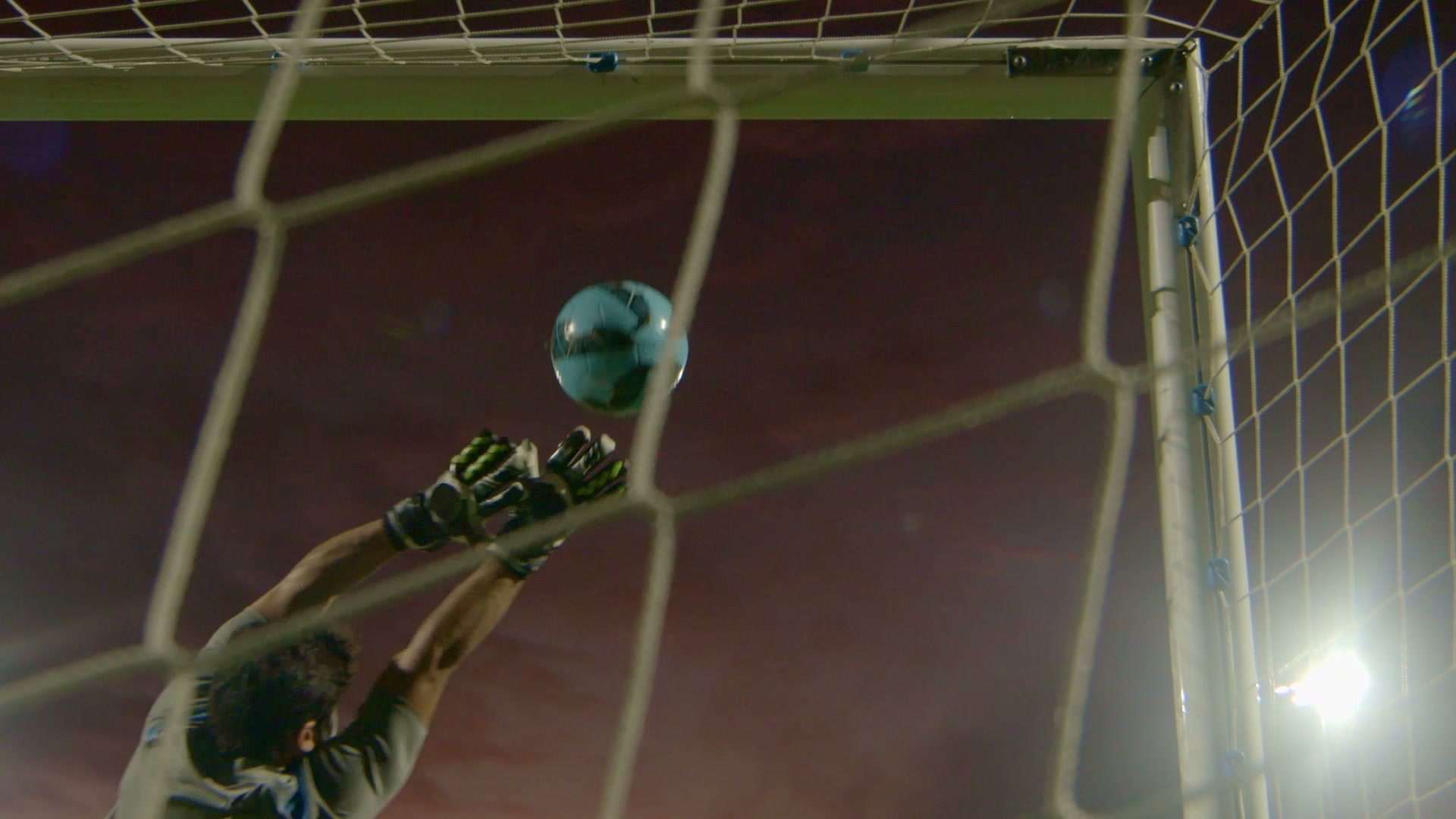 Arquero en plena atajada dentro de un estadio, con la pelota sobre el travesaño