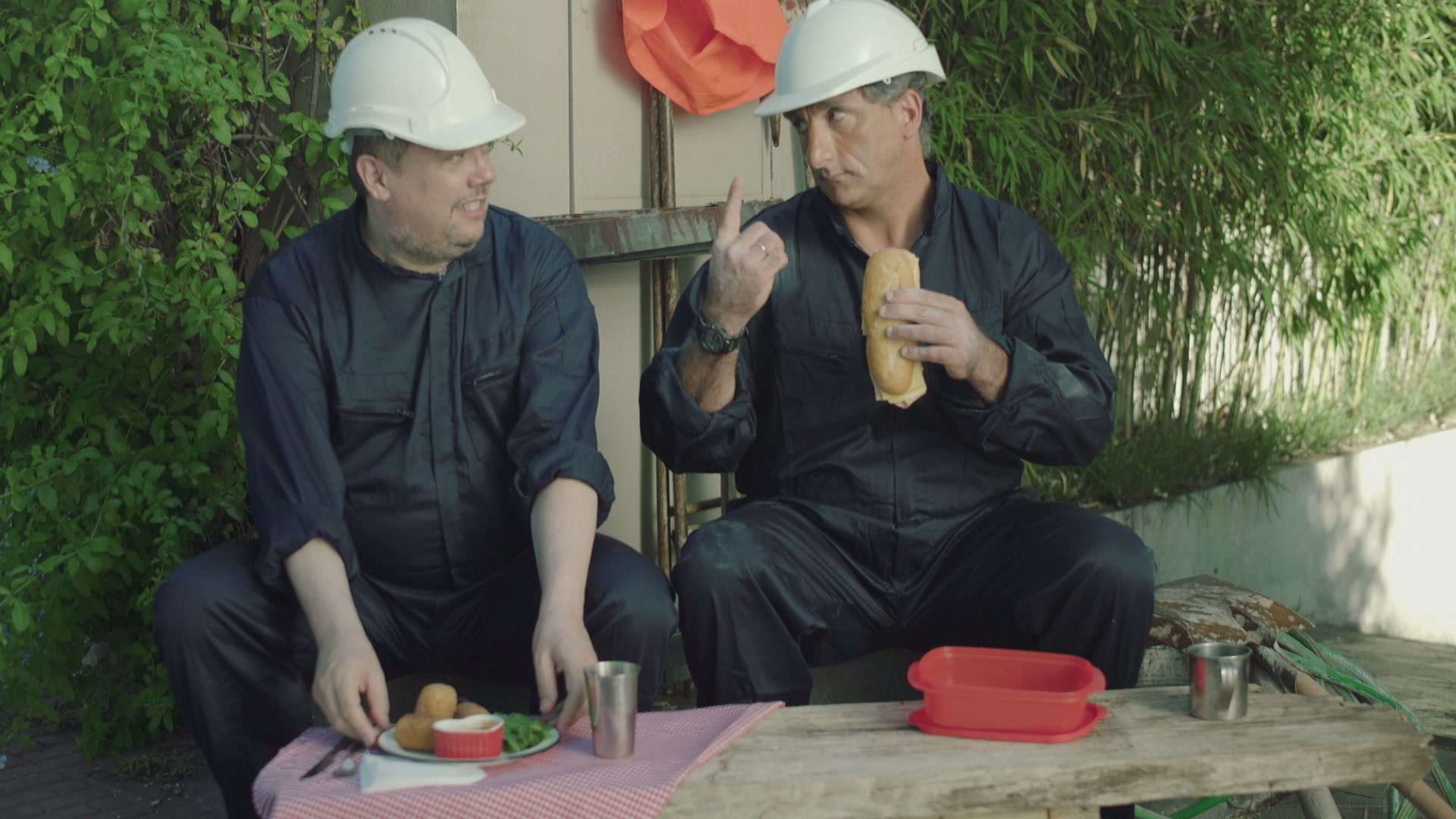 Dos obreros con casco almorzando sentados en un banco al aire libre