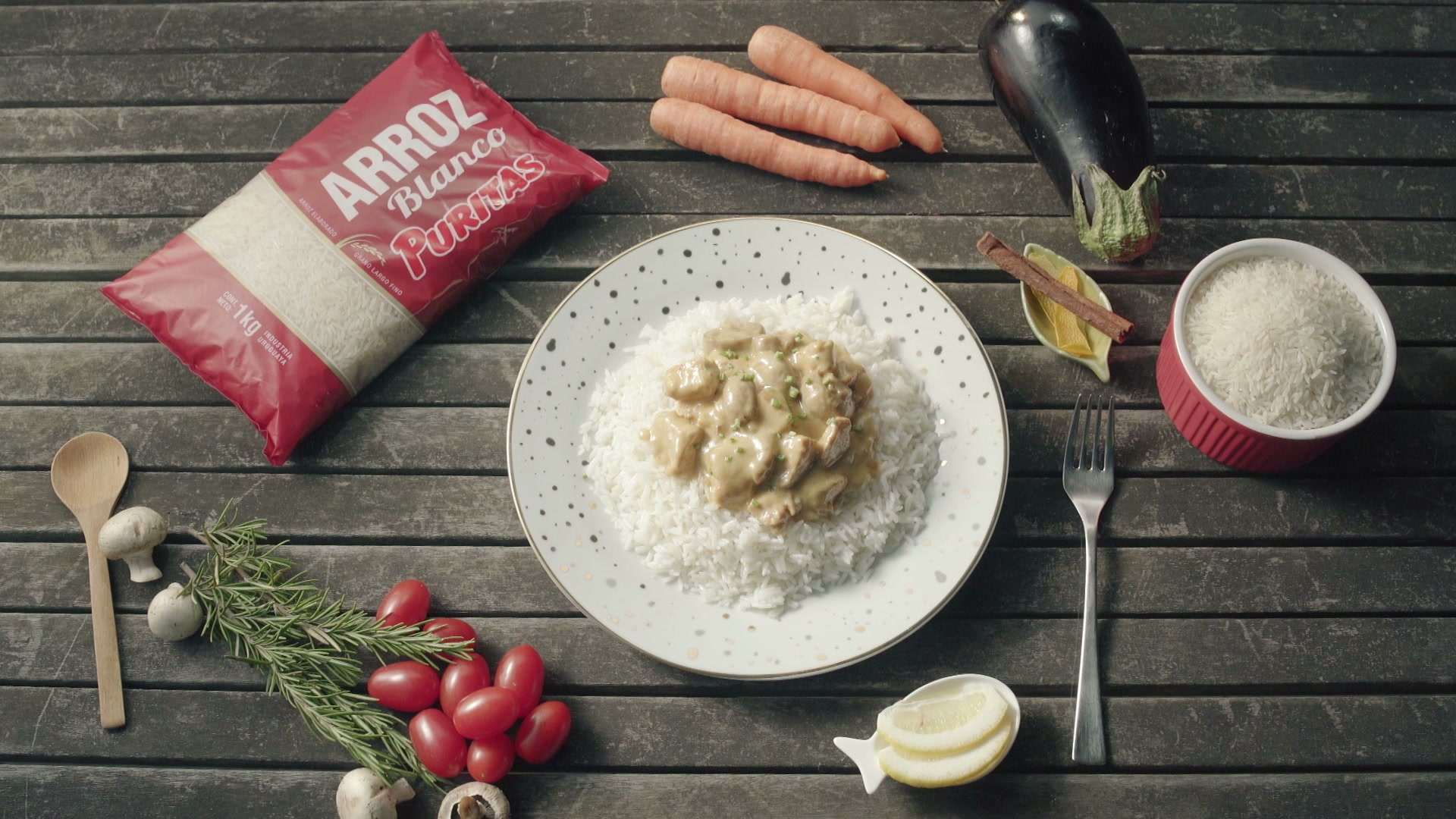 Bolsa de arroz junto a un plato servido, verduras y cubiertos sobre una mesa de madera