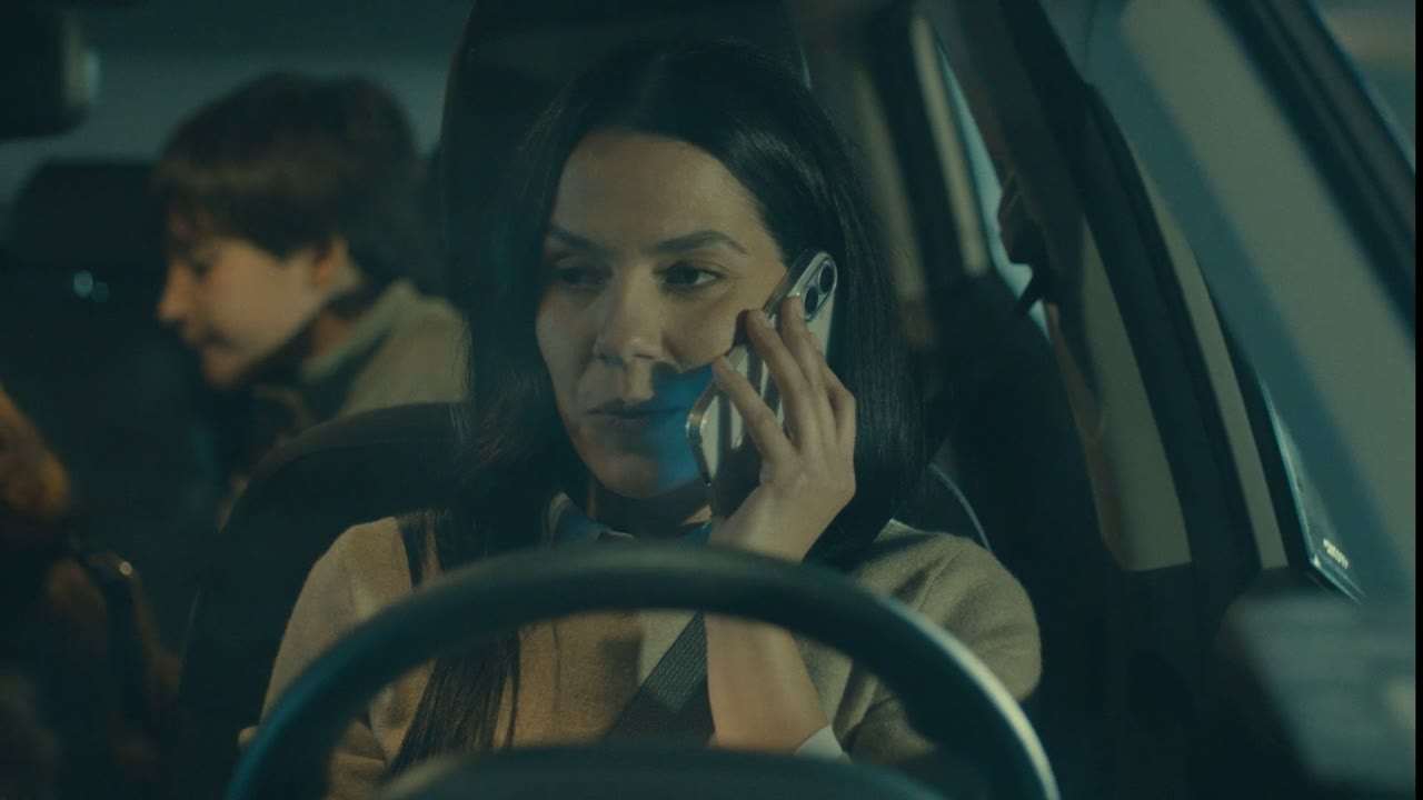 Una mujer al volante de un auto habla por teléfono, con un niño en el asiento de atrás