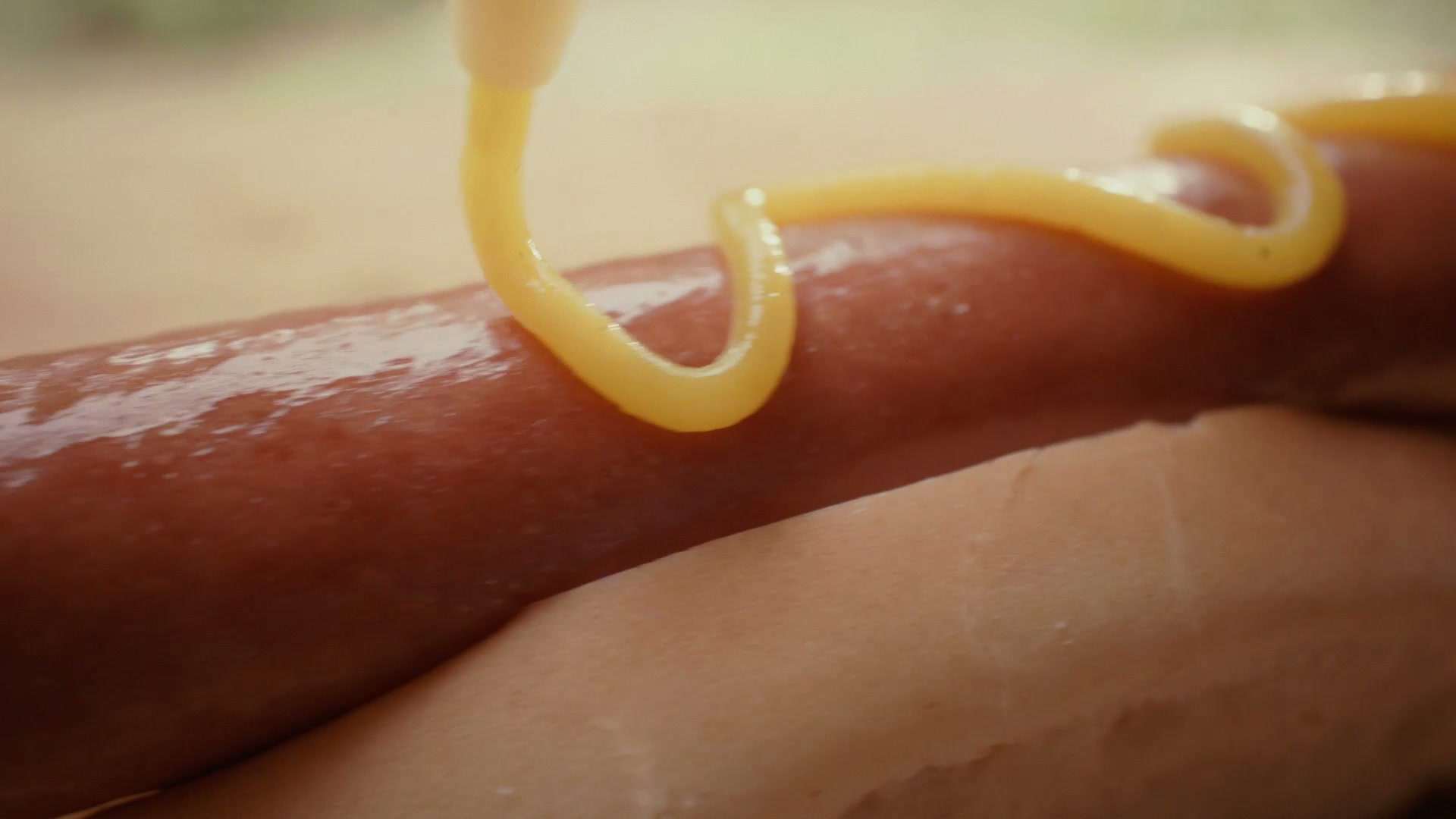 Primer plano de una salchicha con mostaza cayendo en un hilo