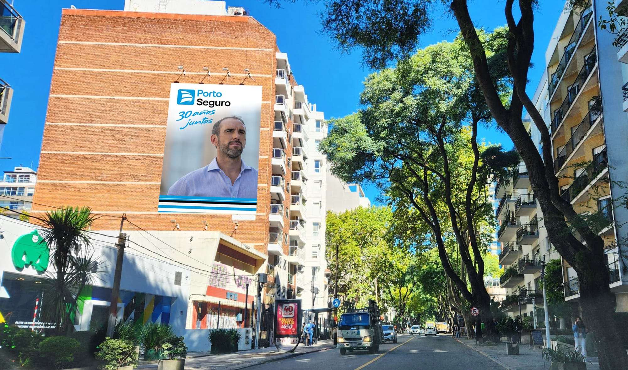 Montaje del gráfico «30 años juntos» con Diego Godín sobre la medianera de un edificio de ladrillo, en una calle arbolada de Montevideo